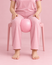 Mini ballon Pilates rose maintenu entre les genoux pendant un exercice assis