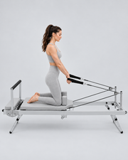 Femme en tenue grise utilisant les sangles du reformer Pilates pliable compact en aluminium gris.