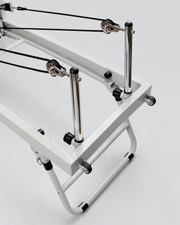 Détail des poulies, cordes et montants du reformer Pilates pliable en aluminium gris.