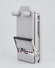 Reformer Pilates pliable compact en aluminium gris, replié de trois quarts.