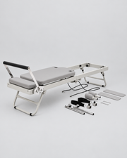 Reformer Pilates en aluminium gris avec ses éléments démontés disposés à côté.