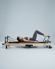 Femme faisant du footwork sur le reformer Pilates pliable Opilat coloris Charbon