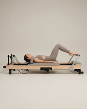 Femme faisant du footwork sur le reformer Pilates pliable Opilat coloris Galet